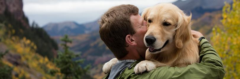 Image of a man and dog sitting outside with a mountain in the background. 