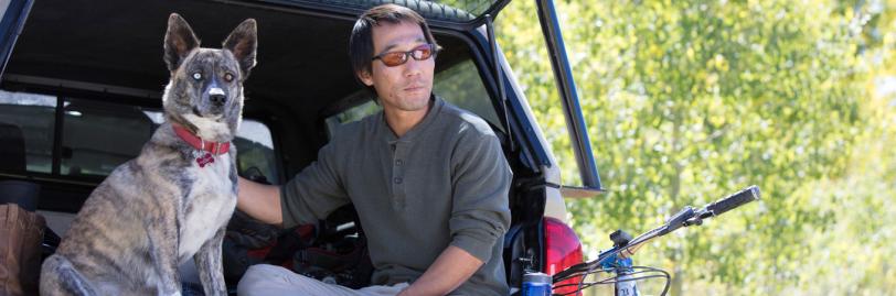 A man and a dog sitting on a tailgate of a car in the woods. 