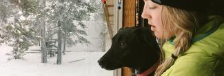 A woman and a dog looking out the window to a snowy yard